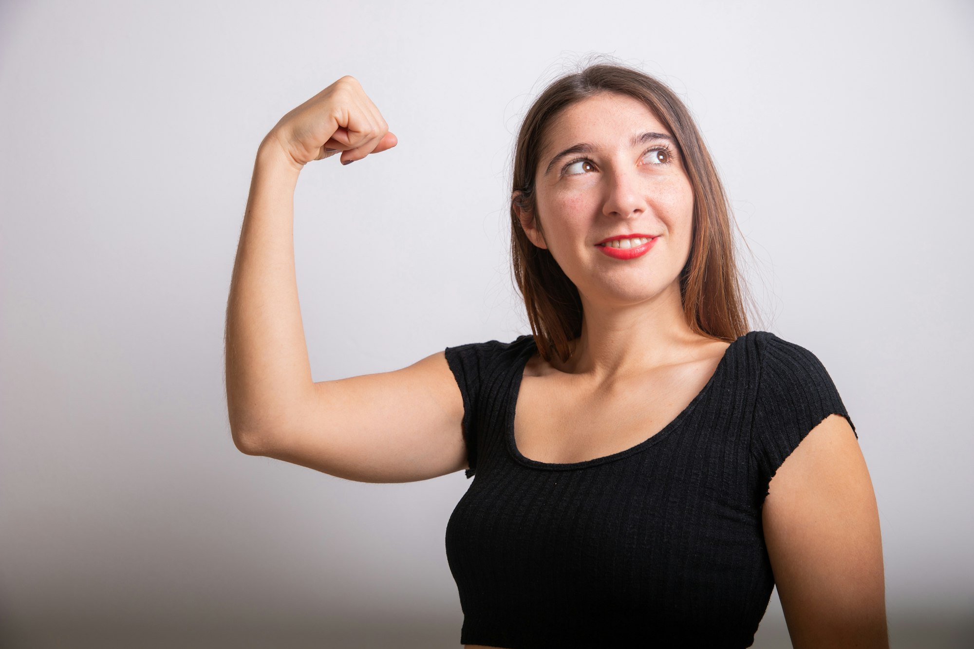 A young woman shows her biceps and looks to the side, concept of women's empowerment