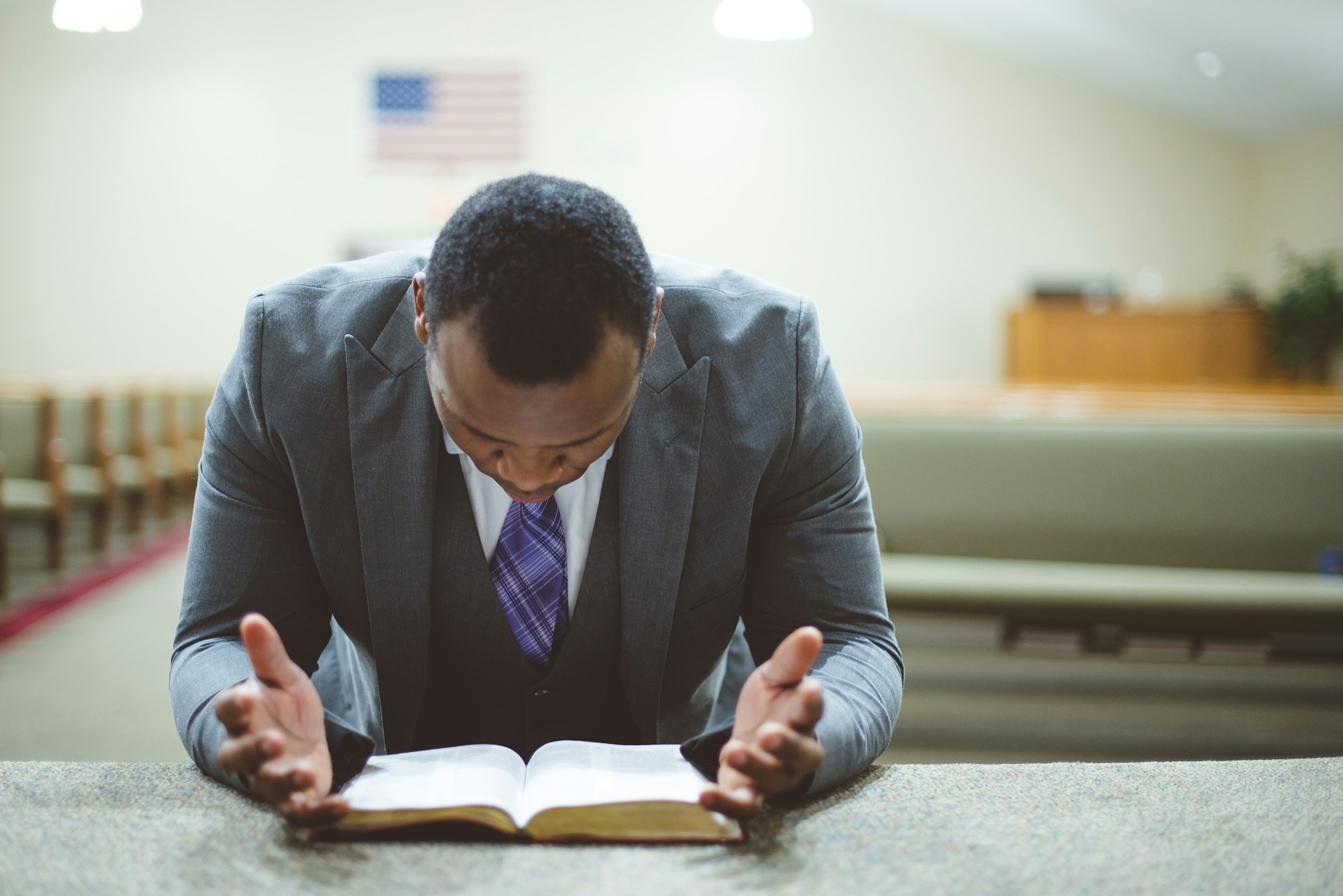 African-American male praying with his head down looking at the Bible at the church