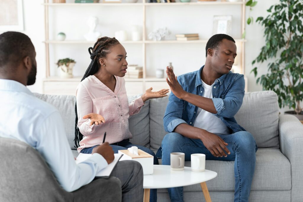 Black couple arguing in front of their therapist at session in office