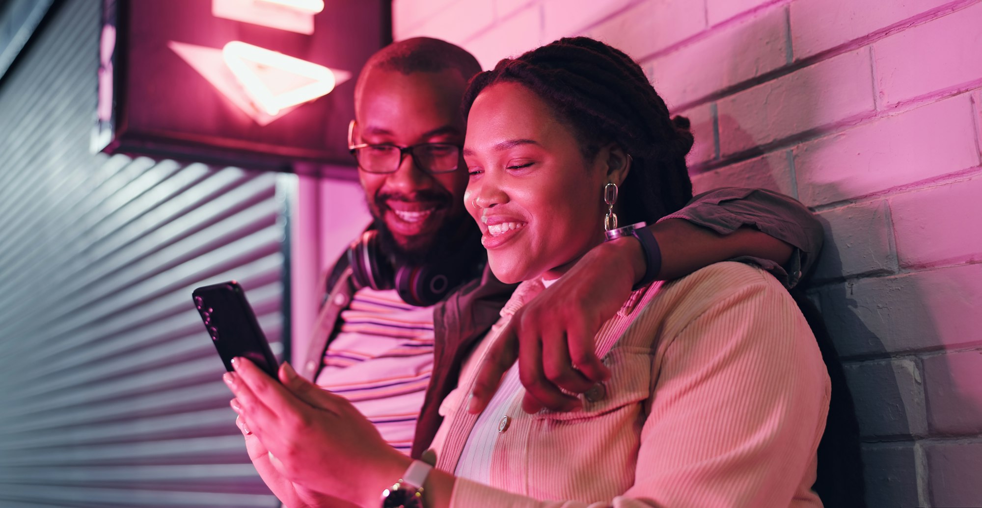 Date, phone and smile with black couple by neon light in city at night together for date, love or r