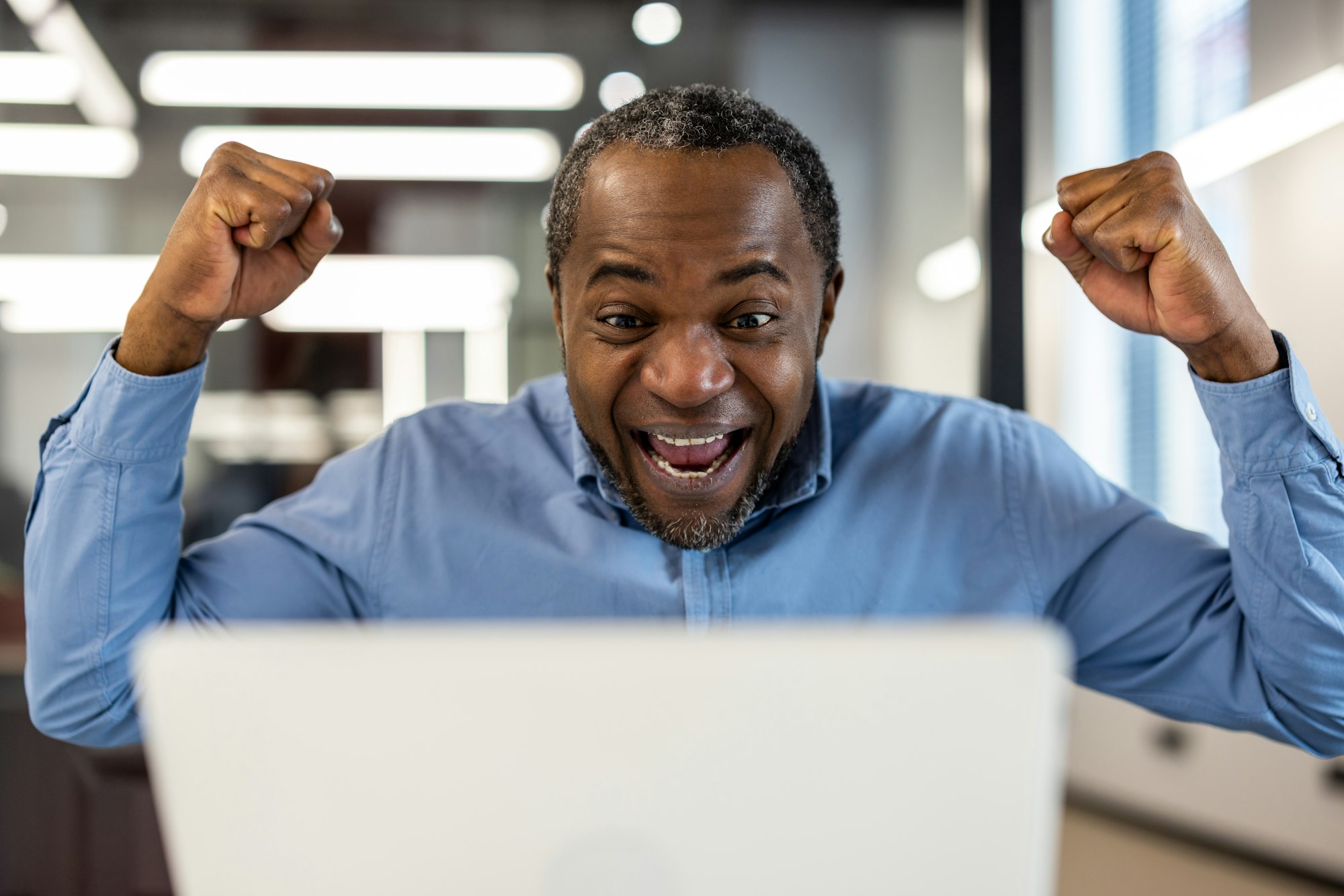 Happy businessman celebrating success at work on laptop in office